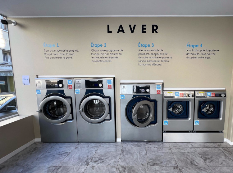 Row of Electrolux Professional self-service washing machines at St Omer Laundromat with customer instructions on wall