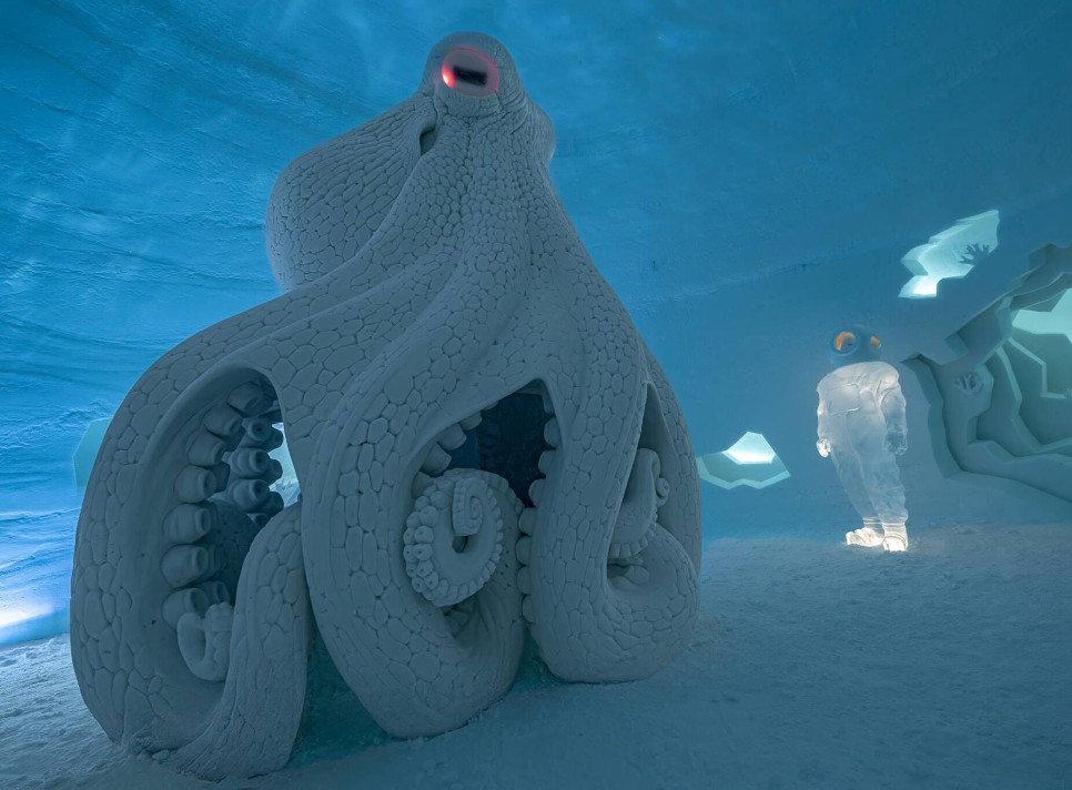 Large ice sculpture of an octopus in an underwater-themed ice exhibit, with a humanoid ice figure in the background.